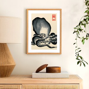 Op de afbeelding: Een ingelijste prent met een zwart-wit illustratie van een octopus. De octopus is afgebeeld in een traditionele Japanse stijl, met gedurfde penseelstreken en een minimalistische esthetiek. De prent zit in een houten lijst.
