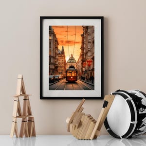May include: A framed photograph of a red vintage tram traveling down a city street at sunset. The tram is in the center of the image, with buildings on either side. The sky is a vibrant orange and pink.