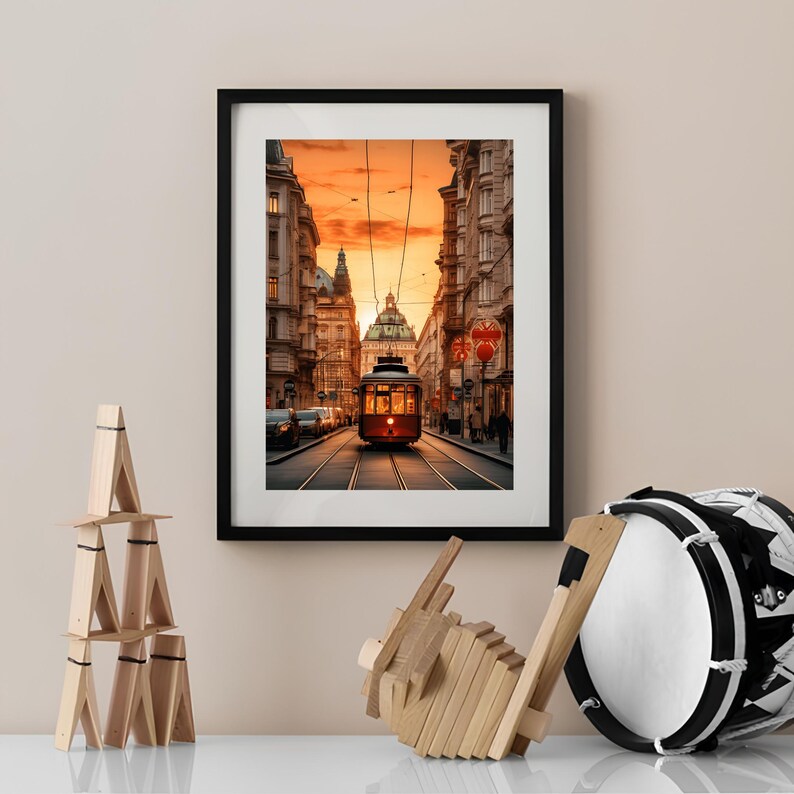 May include: A framed photograph of a red vintage tram traveling down a city street at sunset. The tram is in the center of the image, with buildings on either side. The sky is a vibrant orange and pink.