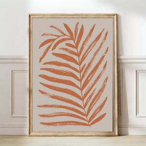 May include: A framed print of a stylized orange leaf on a beige background. The leaf is drawn with thick brushstrokes.
