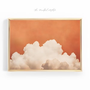 May include: A framed print of a photograph of a large, fluffy white cloud against a bright orange sky. The frame is gold.