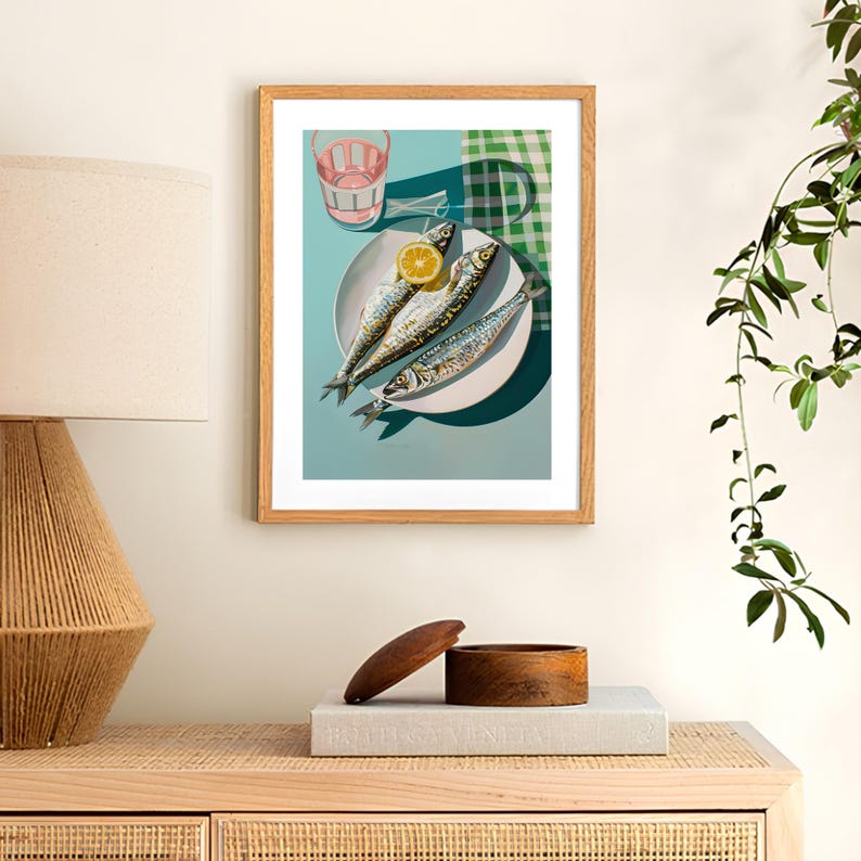 May include: A framed illustration of a plate of three whole fish with a lemon wedge on top, a pink glass, and a green and white checkered tablecloth. The background is a light blue color.