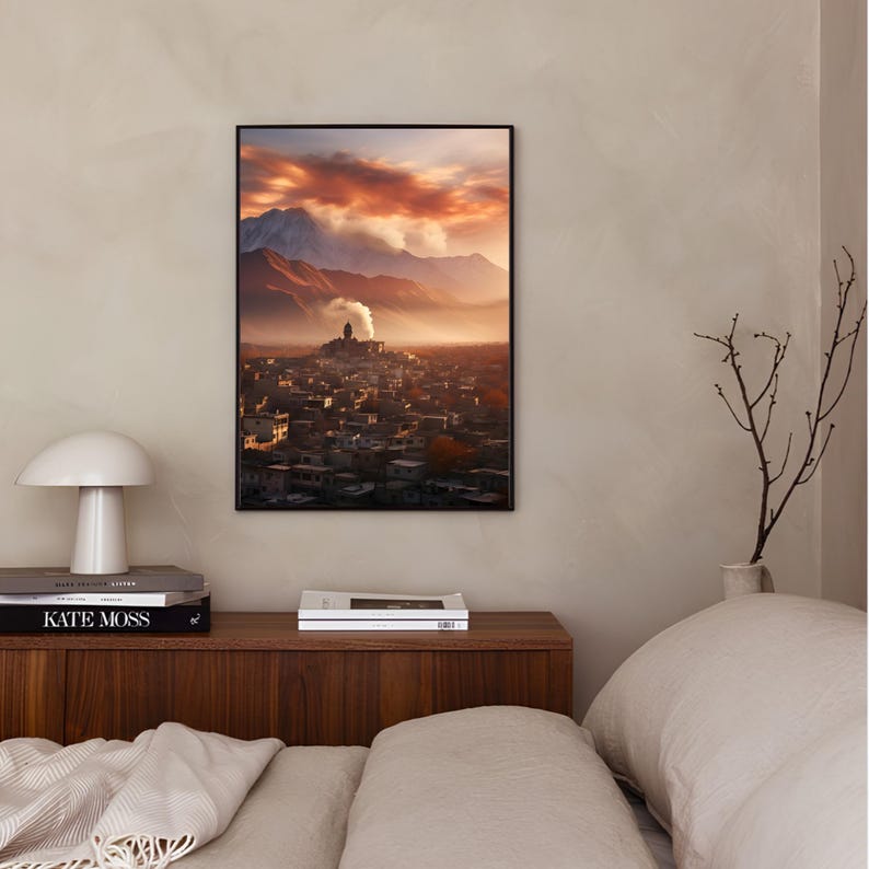 May include: A framed photograph of a mountain village with a red sky and clouds. The village is nestled in a valley with a mountain in the background.