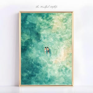 Könnte beinhalten: Ein Aquarellbild von zwei Personen, die in einem türkisfarbenen Meer schwimmen. Das Wasser ist klar und der Himmel ist blau. Das Bild ist in einem goldenen Rahmen gerahmt.