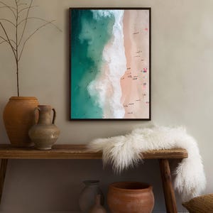 May include: An aerial photograph of a beach with turquoise water and white waves crashing on the shore. The sand is a light pink color and there are many people on the beach.