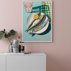 May include: A framed print of a still life featuring three whole fish on a white plate with a lemon slice. The plate is on a turquoise background with a green and white checkered cloth in the background.
