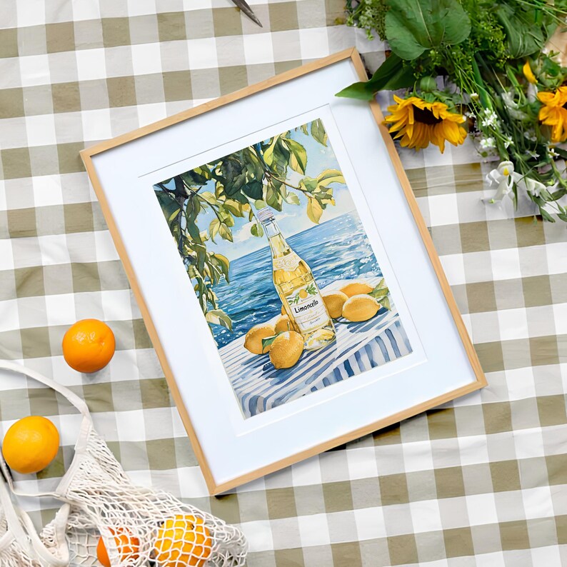 May include: A framed watercolor painting of a bottle of lemonade with lemons and a blue and white striped background. The bottle is labeled "Limoncello" and is surrounded by lemons.