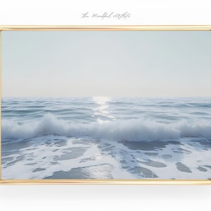 May include: A framed photograph of a seascape with white foamy waves crashing on the shore. The water is a light blue color and the sky is a pale blue. The frame is gold.