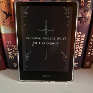 May include: A black Kindle e-reader with a clear protective case. The case has a design of a sword with a rose and the text "Because beasts don't get the beauty".
