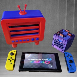 May include: A blue and red retro TV-style game cartridge holder with a blue and purple crate game cartridge holder, two Nintendo Switch controllers, and a Nintendo Switch console displaying the game Mario Kart 8 Deluxe.