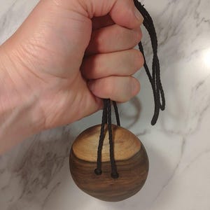 May include: A round wooden pendant with a dark brown wood top and a lighter brown wood bottom. The pendant is attached to a black cord.