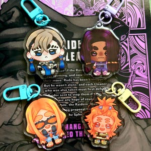 Puede incluir: Cuatro llaveros acrílicos con diseños de personajes de dibujos animados. Cada llavero tiene un personaje diferente con diseños coloridos, adjuntos a cierres de colores. El fondo incluye texto y elementos gráficos morados y negros.