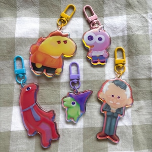 Può includere: Una collezione di sei portachiavi in acrilico colorati con personaggi dei cartoni animati. Ogni portachiavi ha un design unico ed è attaccato a un moschettone in metallo. I portachiavi sono in vari colori, tra cui giallo, rosa, rosso, viola e verde.