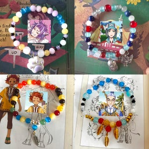 Può includere: Quattro braccialetti colorati con perline e ciondoli. Ogni braccialetto presenta un personaggio diverso di una serie anime o manga. I braccialetti sono esposti su uno sfondo bianco con testo stampato.