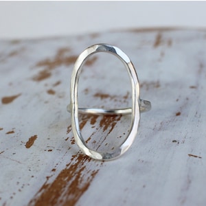 May include: A silver oval ring with a hammered texture. The ring is open and has a smooth, polished finish.