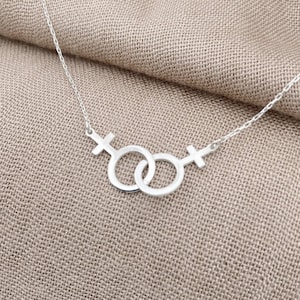 May include: A silver necklace with a linked chain and a pendant featuring two intertwined female symbols.