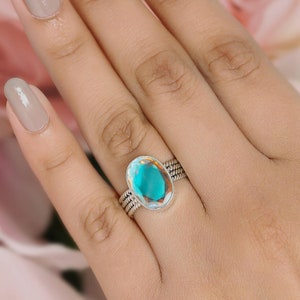 May include: A silver ring featuring a large oval-shaped iridescent gemstone. The gemstone displays a light blue and green hue.