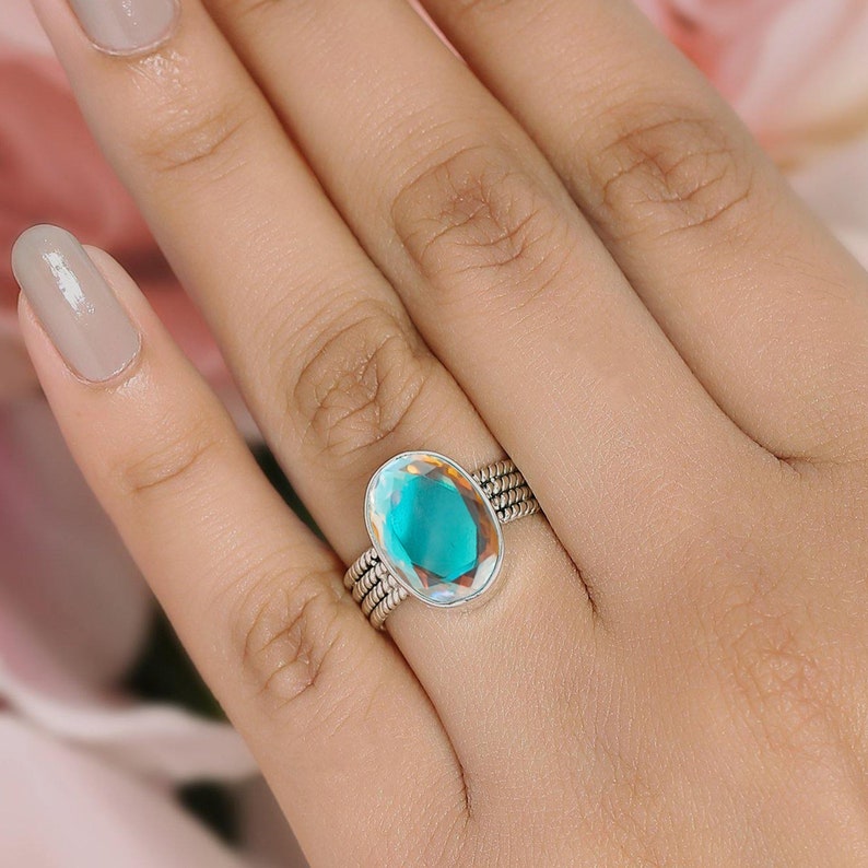 May include: A silver ring featuring a large oval-shaped iridescent gemstone. The gemstone displays a light blue and green hue.