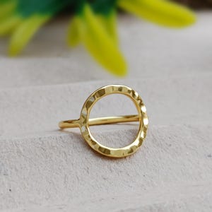 May include: A gold-toned ring with a hammered, circular design. The ring is simple and minimalist.