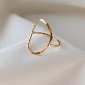 Puede incluir: Un anillo de color dorado con un diseño ovalado martillado. El anillo está abierto y tiene un estilo simple y minimalista.