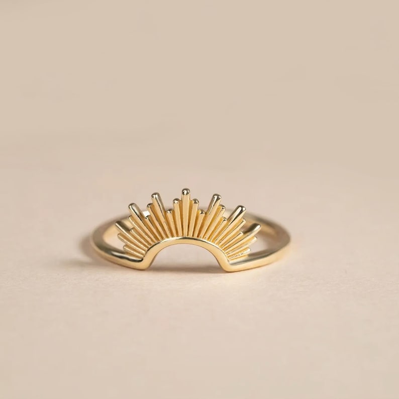 Pu&ograve; includere: Un anello color oro con un design a raggi di sole. L'anello ha una fascia sottile e circolare, mentre l'elemento a raggi di sole &egrave; composto da numerosi raggi verticali, creando un gioiello radioso e accattivante.