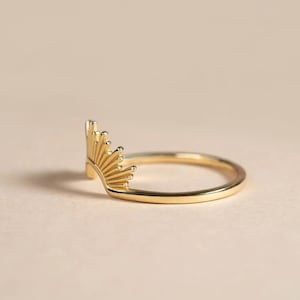 Pu&ograve; includere: Un anello color oro con un design a raggiera. L'anello presenta una fascia delicata e un elemento a raggiera stilizzato, che si irradia verso l'esterno. L'anello &egrave; mostrato su uno sfondo neutro, evidenziando i suoi dettagli intricati.