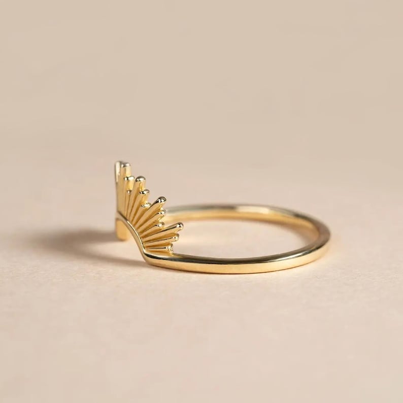 Pu&ograve; includere: Un anello color oro con un design a raggiera. L'anello presenta una fascia delicata e un elemento a raggiera stilizzato, che si irradia verso l'esterno. L'anello &egrave; mostrato su uno sfondo neutro, evidenziando i suoi dettagli intricati.