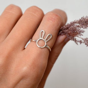 Puede incluir: Un anillo de plata con un diseño de conejo. El anillo está en el dedo de una persona.
