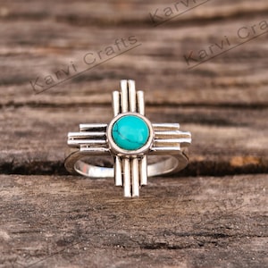 Puede incluir: Anillo de plata con una piedra turquesa en el centro, con forma del símbolo del estado de Nuevo México.