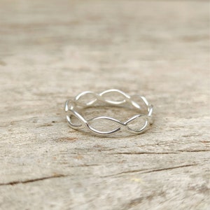 Puede incluir: Un anillo de plata con un diseño delicado e entrelazado. El anillo está hecho de metal liso y pulido y tiene un estilo simple y elegante.