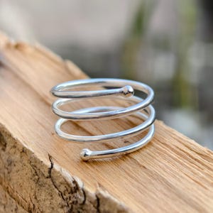 May include: A silver spiral ring with a rounded end. The ring is made of multiple bands of silver that are twisted together to create a spiral shape.