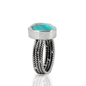 May include: A silver ring with a turquoise gemstone set in a bezel setting. The band is made of twisted silver wire.