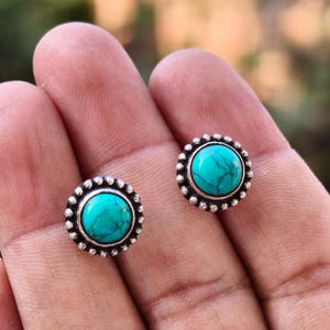 Può includere: Un paio di orecchini d'argento con pietre turchesi incastonate in un design circolare.