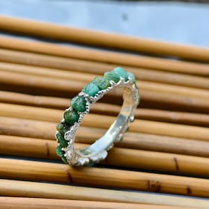 May include: A silver ring with a band of rough, green emerald stones.