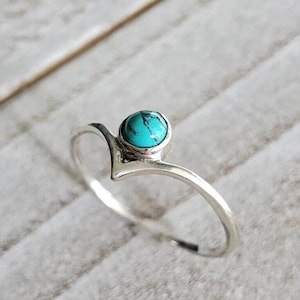 May include: A silver ring with a turquoise gemstone set in a simple, modern design. The ring has a pointed, V-shaped band.