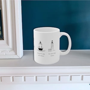 May include: White ceramic mug with black line drawings of lighthouses and the text "Spring Point Ledge South Portland" and "Ram Island Ledge Portland".