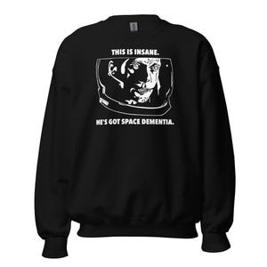 Op de afbeelding: Zwart sweatshirt met een witte afbeelding van een astronautengezicht in een helm. De tekst "This is insane. He's got space dementia." staat onder de afbeelding.