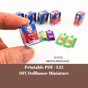 May include: Miniature apple juice boxes and pouches. The apple juice box has a red and blue design with a baby's face and the word "APPLE". Other boxes and pouches are visible in the background. The image also includes the text "Printable PDF 1:12 DIY Dollhouse Miniature".