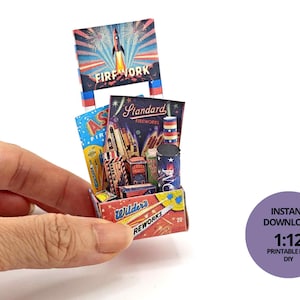 May include: Miniature fireworks display with a rocket graphic on a sign that reads "FIREWORK". The display includes boxes and canisters with colorful labels. The box is held in a hand. The sign reads "INSTANT DOWNLOAD 1:12 PRINTABLE FILE DIY".