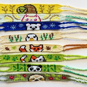 Puede incluir: Una colección de pulseras de la amistad hechas a mano con diseños de animales. Cada pulsera presenta un animal diferente, incluyendo un caracol, un gato, un oso, un pato, un zorro, un panda y un carlino. Las pulseras están hechas de hilos coloridos y tienen un lazo y un extremo trenzado.
