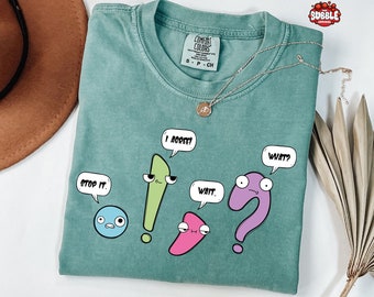 Può includere: Una t-shirt blu turchese con una stampa grafica di quattro segni di punteggiatura dei cartoni animati con fumetti. I fumetti dicono "Stop it", "I agree", "Wait", e "What?" La maglietta ha un'etichetta che dice "Comfort Colors" e "S-P-CH".