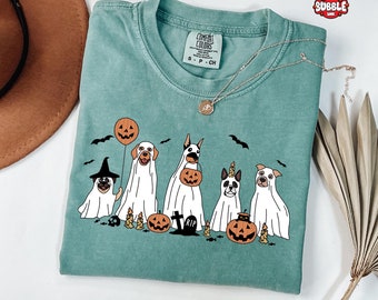 May include: A teal blue t-shirt with a graphic of five dogs dressed as ghosts for Halloween. The dogs are wearing ghost costumes with a pumpkin, a witch's hat, and a unicorn horn. The text "COMFORT COLORS" is on the tag.
