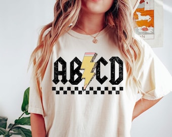 May include: A white t-shirt with a black and yellow lightning bolt graphic and the text "ABCD" in black. The lightning bolt is stylized to look like a pencil.