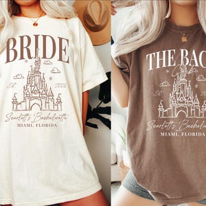 two women wearing t-shirts with the same design, which appears to be a graphic or illustration of a castle or palace. The text on the t-shirts reads "Bridal" and "The Bach" along with the location "Scottish Bachelorette Miami, Florida".