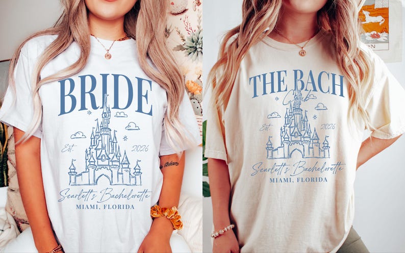 two women wearing white t-shirts with blue text and graphics. The text on the t-shirts reads "BRIDE" and "THE BACH" along with a castle illustration. The t-shirts also have the text "Seattle's Bachelorette" and "MIMI, FLORIDA" printed on them.