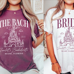 two women wearing t-shirts with the same design, which appears to be a castle or palace-themed design. The t-shirts are purple and white in color.