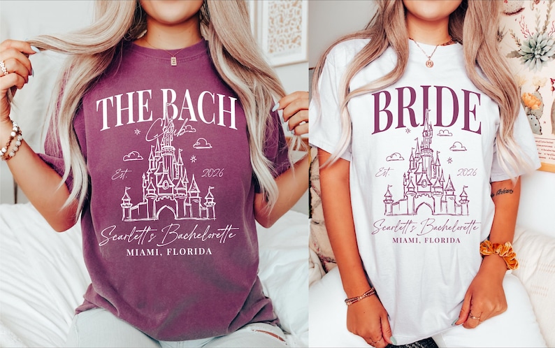 two women wearing t-shirts with the same design, which appears to be a castle or palace-themed design. The t-shirts are purple and white in color.