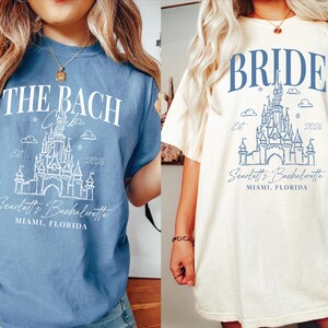 two women wearing t-shirts with a castle design and text related to a wedding or bachelorette party.