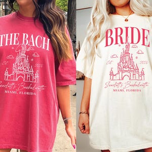 two women wearing t-shirts with the same design, featuring a castle and the text "The Bach" and "Bridal" printed on them.