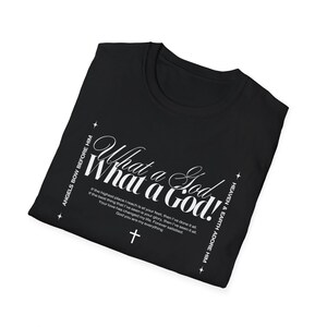 Può includere: T-shirt nera con testo bianco che recita "What a God!" e testo aggiuntivo. La maglietta presenta anche una grafica a croce. Il testo include frasi come "Angels bow before Him" e "Heaven & Earth adore Him."